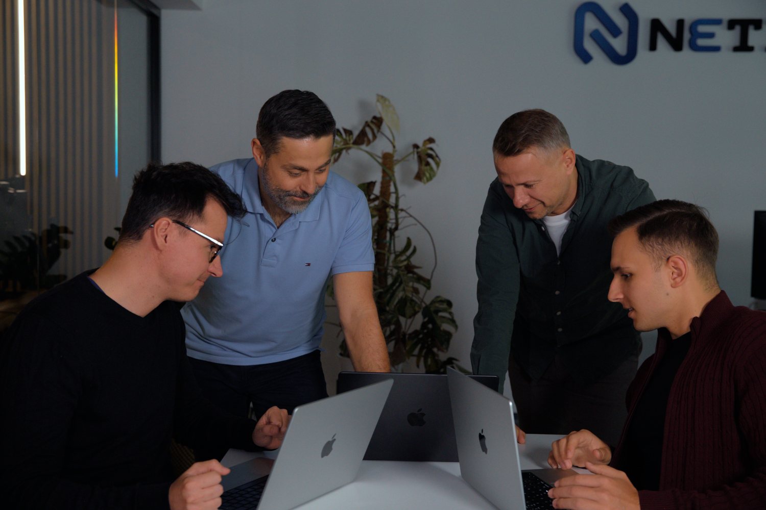 Zespół NETIM pracuje przy laptopach, w tle logo firmy